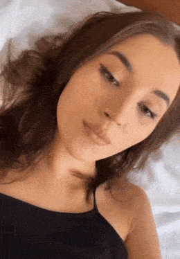 a woman in a black tank top is laying on a bed and looking at the camera