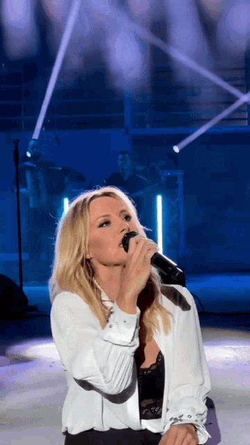 a blonde woman singing into a microphone with a band in the background