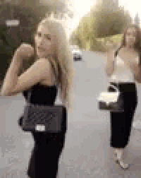 two women are standing next to each other on a street holding handbags .