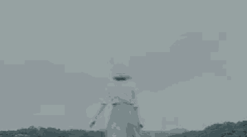 a woman in a white dress and hat is standing on top of a hill .