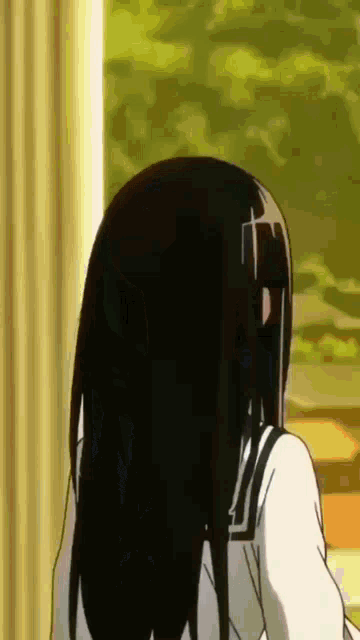a girl with long black hair is standing in front of a window looking out .