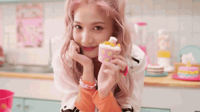 a girl with pink hair is holding a cupcake in her hands