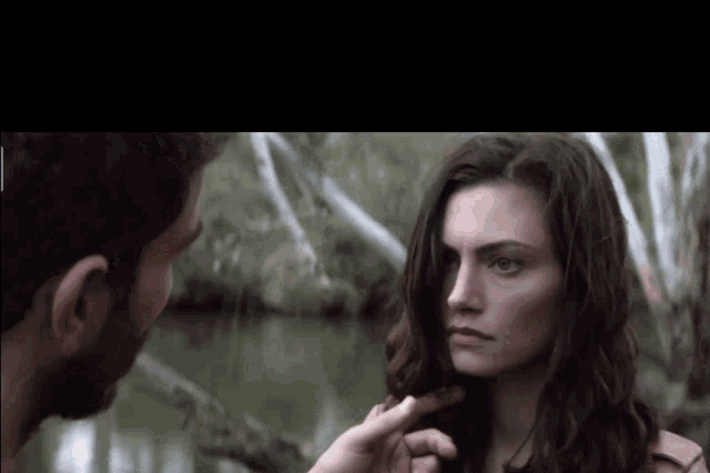 a man touches a woman 's face in front of trees