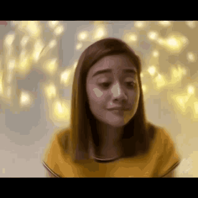 a woman in a yellow shirt is making a funny face in front of a string of lights .