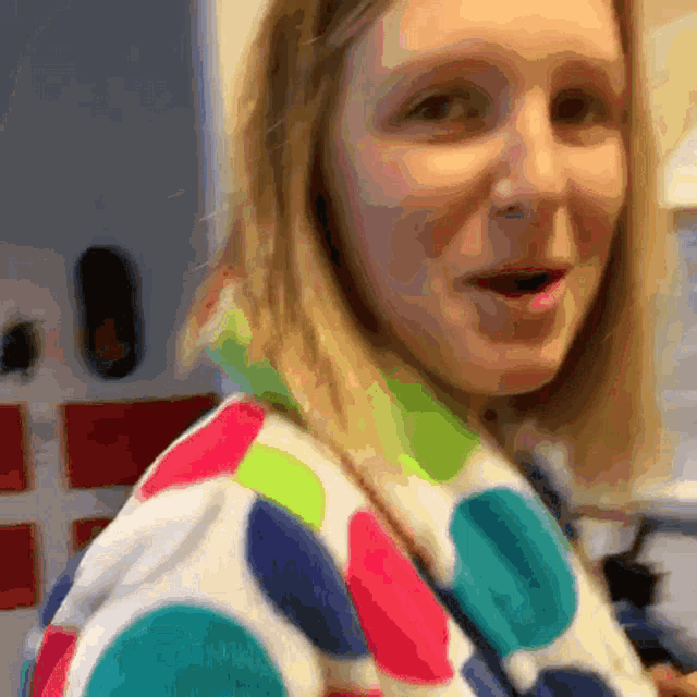 a woman wearing a colorful polka dot sweater looks at the camera