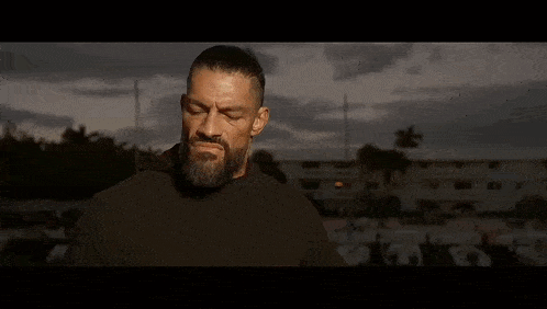 a man with a beard is standing in front of a man with his hands folded .
