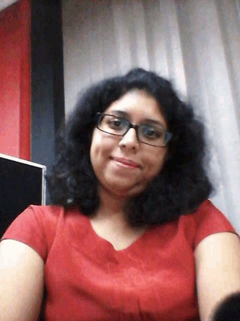 a woman wearing glasses and a red shirt takes a selfie