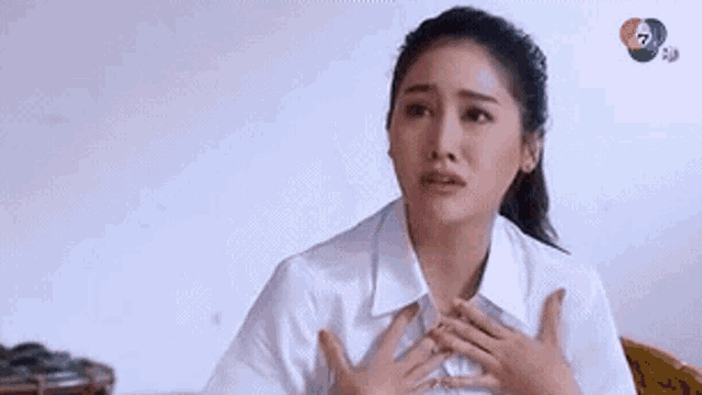 a woman in a white shirt is holding her chest with both hands .