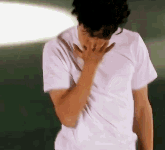 a man wearing a white t-shirt is covering his face with his hands .