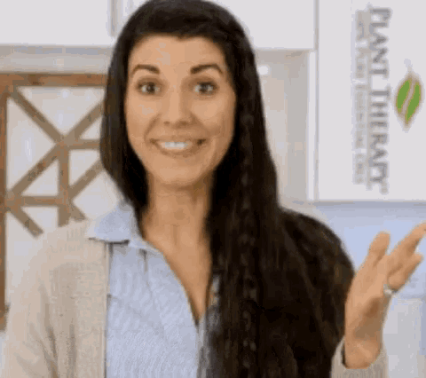 a woman with long dark hair is smiling and waving at the camera .