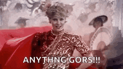 a woman in a red dress is standing in front of a crowd and says `` anything goes ! ''