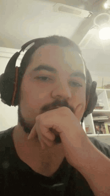 a man with a beard is wearing headphones and covering his mouth with his hand
