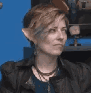 a woman with short hair and elf ears is wearing a leather jacket and earrings .