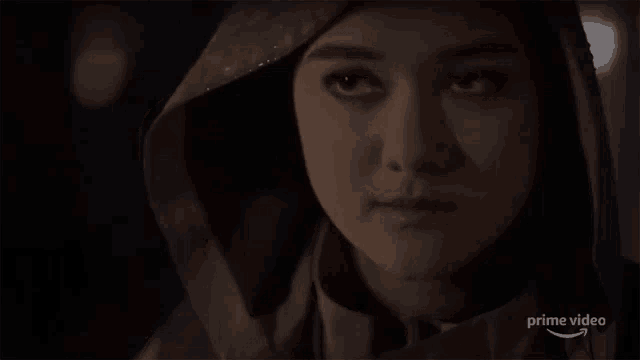 a close up of a woman 's face in a dark room with a hood on her head .
