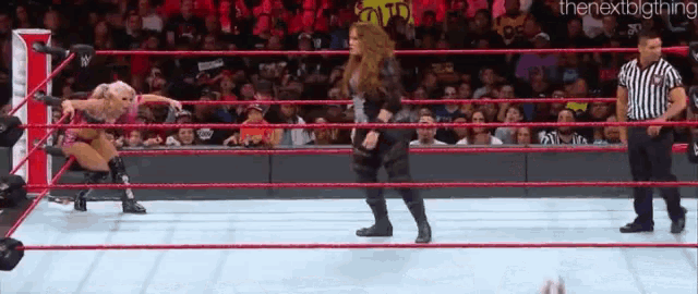 two women are wrestling in a wrestling ring while a referee looks on .
