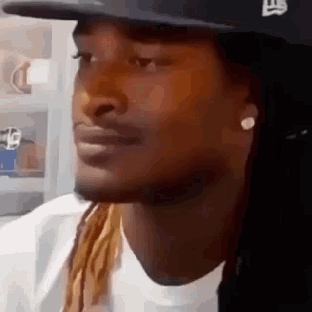 a man with dreadlocks is wearing a hat and earrings and looking at the camera .