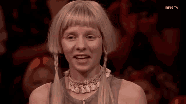 a woman with blonde hair and braids is smiling in front of a tv screen that says nk tv