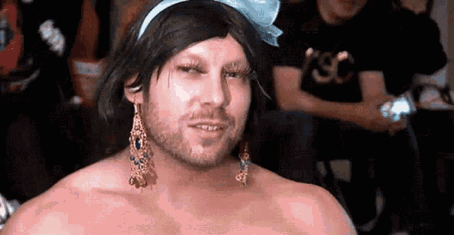 a man with a beard and earrings is wearing a wig and a bow on his head .