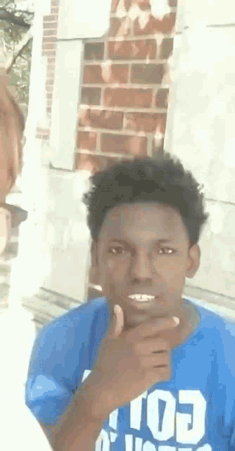 a young man in a blue shirt is making a funny face while standing in front of a brick wall .