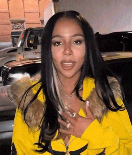 a woman wearing a yellow jacket with a fur hood is standing next to a car .