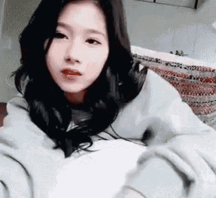 a woman is sitting on a couch wearing a white shirt and a gray sweatshirt .