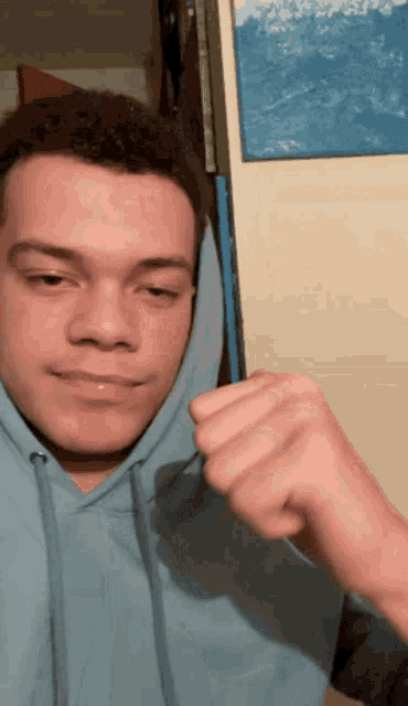 a young man wearing a blue hoodie with a fist in his hand