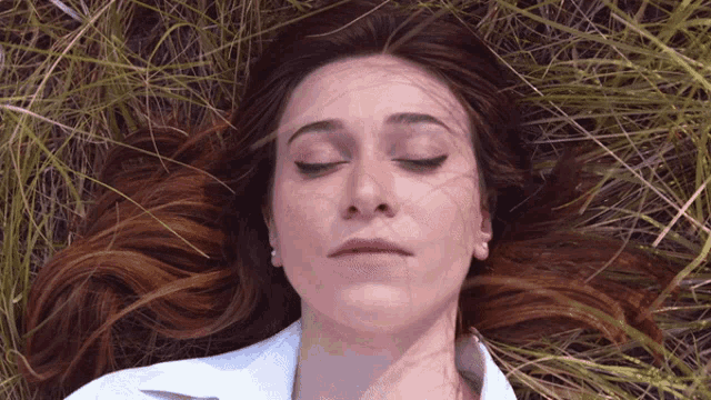 a woman with her eyes closed laying in the grass