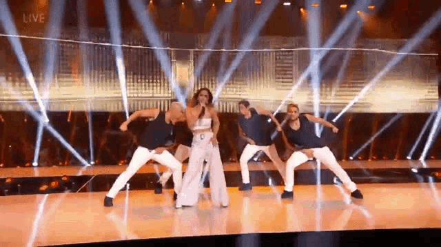 a group of dancers are dancing on a stage with a woman singing into a microphone .