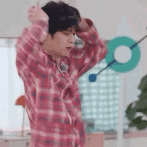 a man wearing a plaid shirt and a hat is standing in a room with his hands on his head .