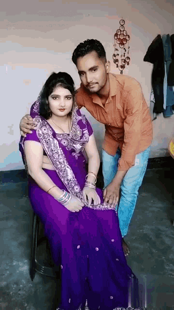 a woman in a purple saree sits next to a man