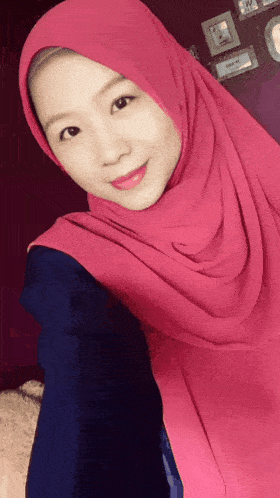 a woman wearing a pink hijab and a blue shirt is smiling