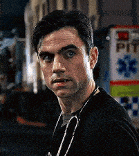 a man wearing a black shirt and a stethoscope around his neck is standing in front of an ambulance .