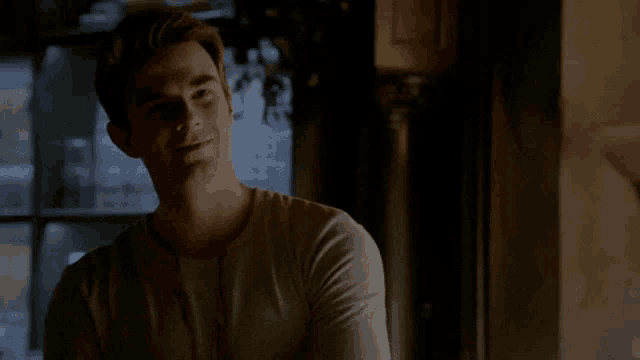 a man in a white shirt is sitting in a dark room looking at something .