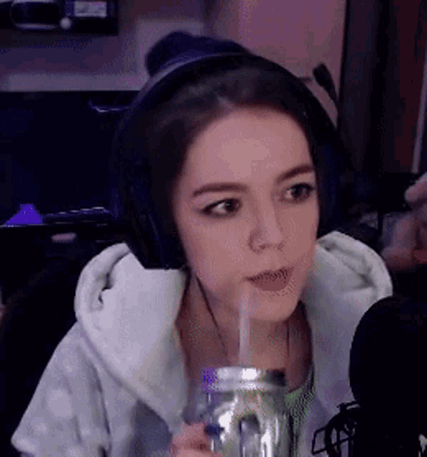 a woman wearing headphones is drinking through a straw from a jar .