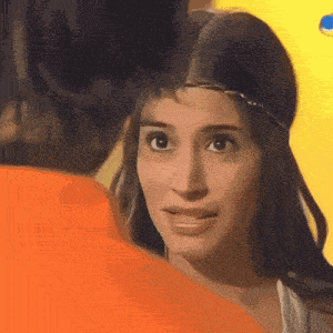 a woman with a crown on her head looks at a man in an orange shirt