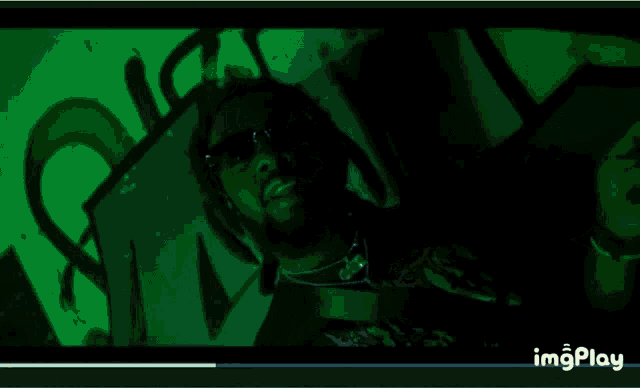 a man wearing sunglasses is standing in front of a wall with graffiti on it that says ou