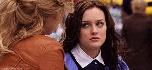 two women are standing next to each other and looking at each other . one of the women is wearing a leather jacket .