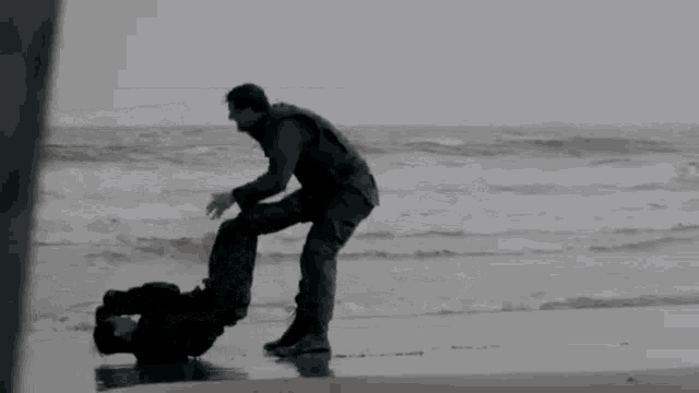 a man is squatting on the beach next to the ocean .