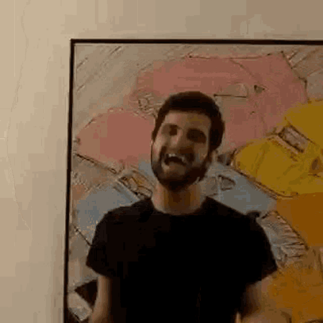 a man with a beard is standing in front of a framed painting on a wall .