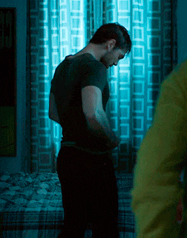 a man in a black shirt is standing in front of a window with blue curtains