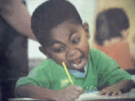 a boy in a green shirt is writing with a yellow pencil in his mouth .
