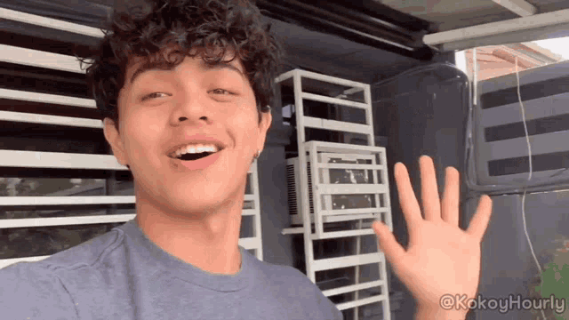 a young man with curly hair is waving his hand in front of a window