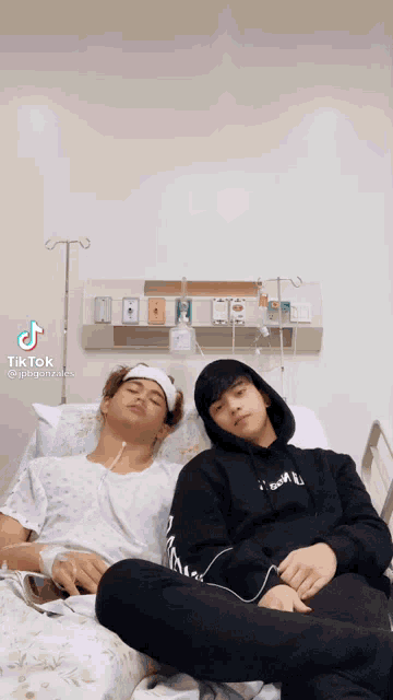 two men are laying in a hospital bed and one has a headband on