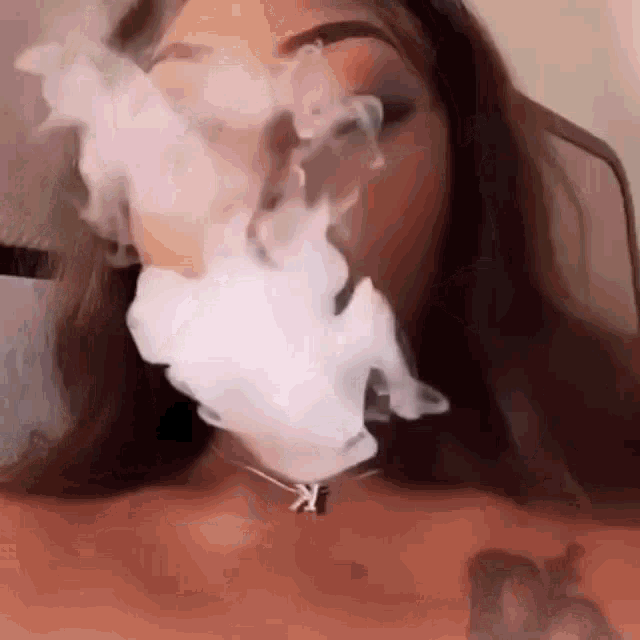 a woman is smoking a hookah and blowing smoke out of her mouth .