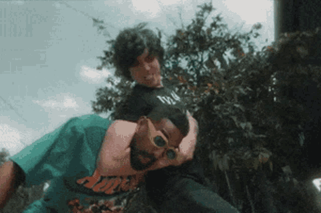 a man wearing sunglasses is laying on another man 's shoulder