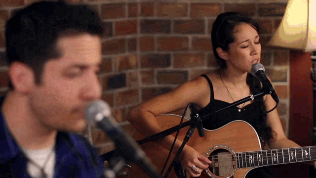 a man sings into a microphone while a woman plays a guitar