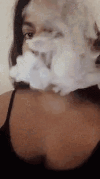 a woman in a black tank top is blowing smoke out of her mouth .