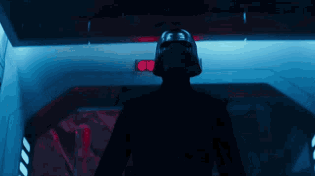 a man in a helmet is standing in a dark room with red lights behind him