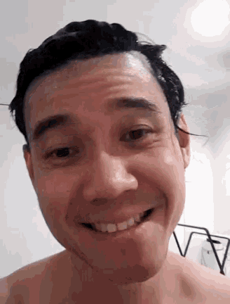 a man without a shirt is smiling and making a funny face while washing his hair .