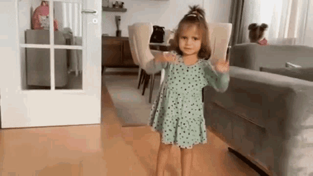a little girl is standing in a living room in front of a couch .